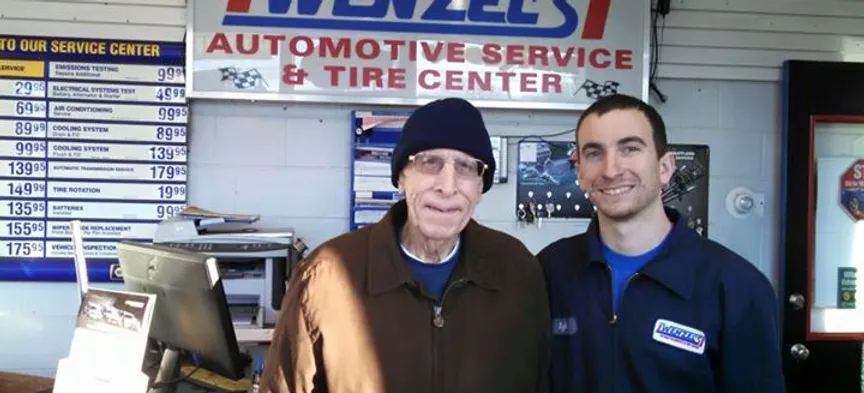 Two members of the Wenzel's team at the service counter under the Wenzel's Automotive Service and Tire Center sign