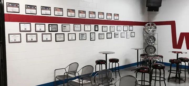 Customer waiting area at Wenzel's Automotive with framed certificates on the wall and tire wheels on display